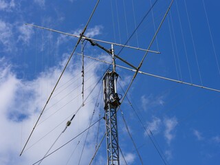 A close-up of a ham radio antenna with stay ropes against a cloudy blue sky