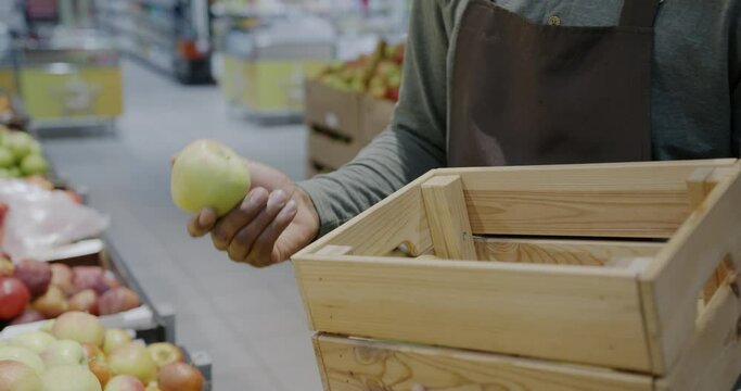 Close-up of male hand putting apples in wooden box while salesman packing fruit for delivery in supermarket. Retail store and food concept.