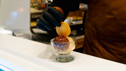 Barista decorates crackers on top of chocolate gelato in glass