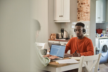 Young multiracial couple working online from home in their kitchen