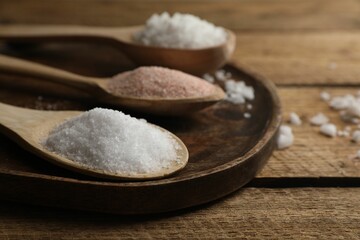 Different natural salt in spoons on wooden table, closeup. Space for text