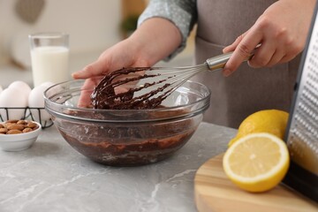 Woman mixing chocolate cream with whisk in bowl at gray marble table indoors, closeup