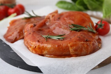 Board with raw marinated meat and rosemary on light table, closeup