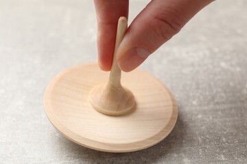 Woman playing with wooden spinning top at grey textured background, closeup