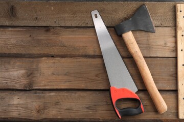 Saw with colorful handle and axe on wooden background, flat lay. Space for text