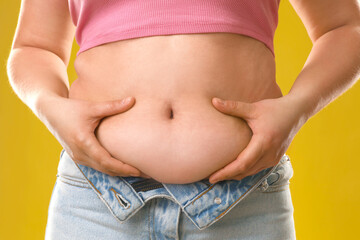 Fototapeta premium Woman touching belly fat on goldenrod background, closeup. Overweight problem