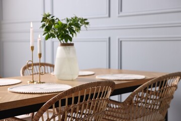 Rattan chairs, table, burning candles and vase with green branches in stylish dining room