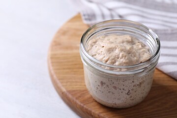 Sourdough starter in glass jar on light table, closeup. Space for text