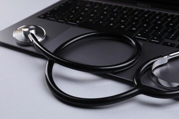 Laptop and stethoscope on light grey background, closeup