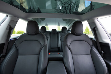 Panoramic glass sun roof in the modern electric car interior. The view from the empty car with seats. Luxury car leather seats. Interior of new clean expensive car. Passenger seats with leather - obrazy, fototapety, plakaty