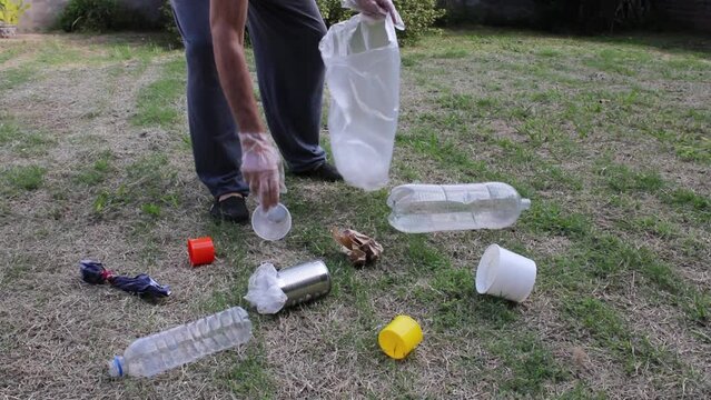 Reciclado de basura plástica y metálica en el parque. El hombre recoge desechos plásticos y metálicos en el parque de la ciudad, con guantes para ser reciclados y no contaminen el ecosistema.