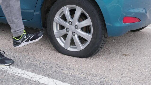 Close-up of a flat tire on a car. The man checks and kicks the wheel.