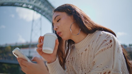 Relaxed woman surfing phone at sunny river bank closeup. Girl sipping coffee