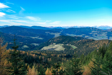Panoramic view of snow capped mountain ridges of Woelzer Tauern seen from Grebenzen, Gurktal Alps, Styria, Austria. Calm serene atmosphere in Austrian Alps. Idyllic forest in foreground. Wanderlust