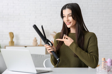Beautiful young happy female blogger with laptop and curling on recording video at home