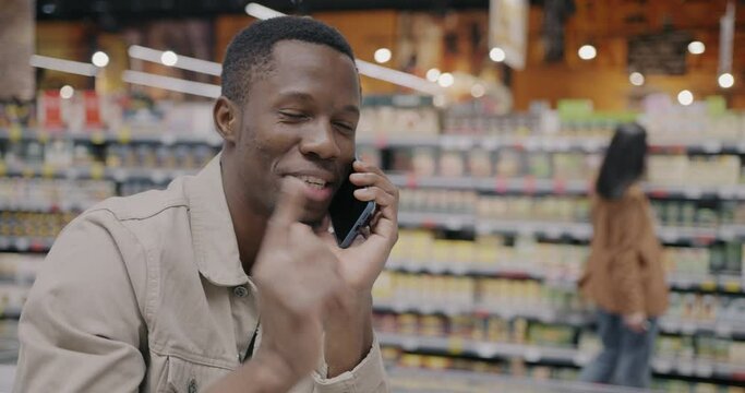 African American man satisfied customer speaking on mobile phone discussing purchase in supermarket. Cellphone communication and shopping concept.