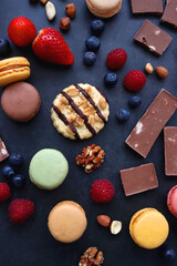 Fototapeta na wymiar Macarons, chocolate, cookies, berries and various nuts on dark blue background. Top view.