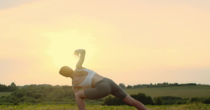 Young woman doing yoga in nature, wearing a white top and olive-colored shorts.