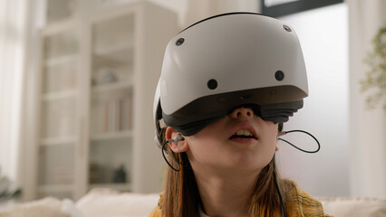 Surprised amazed Caucasian girl kid child schoolgirl playing online video game in 3D world metaverse using virtual reality helmet at home play gaming controller explore cyberspace wearing VR glasses