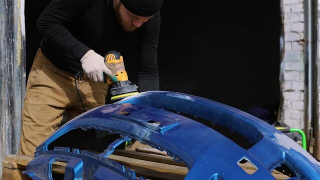 man repairing bumper, sanding paint for painting, repairing cracked bumper.