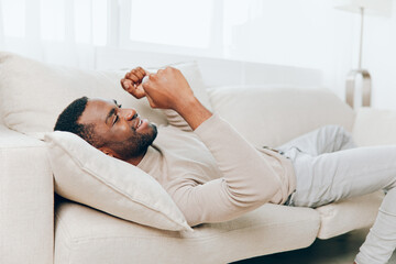 Stressed African American man with a headache sitting alone on the couch at home He looks tired,...