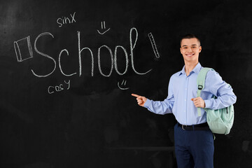 Male student with backpack pointing at word SCHOOL written on blackboard. End of school concept