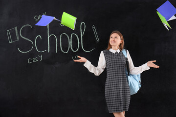 Female student throwing copybooks away near word SCHOOL written on blackboard. End of school concept