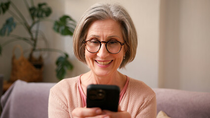 Happy mature old 60s woman, older middle aged female holding smartphone using mobile app, texting...