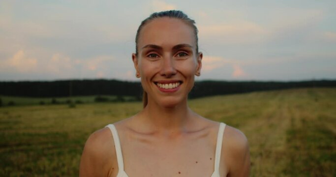 Young woman doing yoga in nature, wearing a white top and olive-colored shorts.