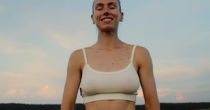Young woman doing yoga in nature, wearing a white top and olive-colored shorts.