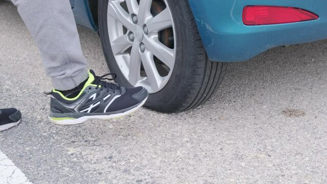 Close-up of a flat tire on a car. The man checks and kicks the wheel.