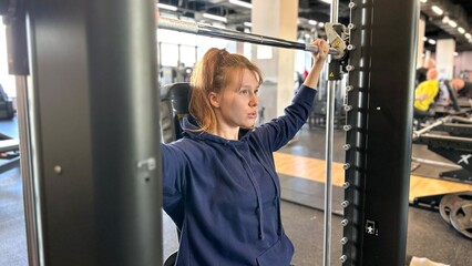 young positive woman working out on a smith machine, doing back and arm exercises, positive, gym