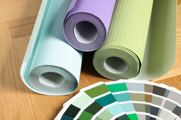 Different wallpaper rolls and color palette samples on wooden table