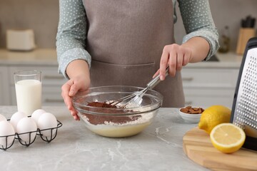 Woman making chocolate dough with whisk in bowl at gray marble table, closeup