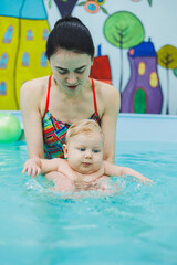 Obraz na płótnie Canvas Trainer teaches baby to swim, swimming pool for children. Child development.