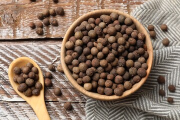 Aromatic allspice pepper grains in bowl and spoon on wooden table, top view