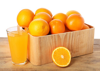 Fresh oranges in crate and glass of juice on wooden table against white background