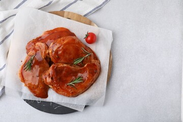 Board with raw marinated meat, rosemary and tomato on light table, top view. Space for text
