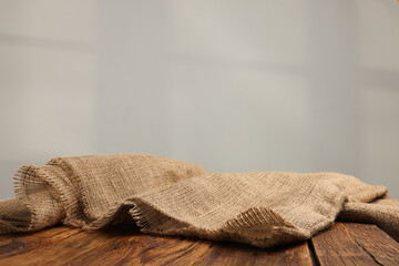 Natural burlap fabric on wooden table against light background. Space for text