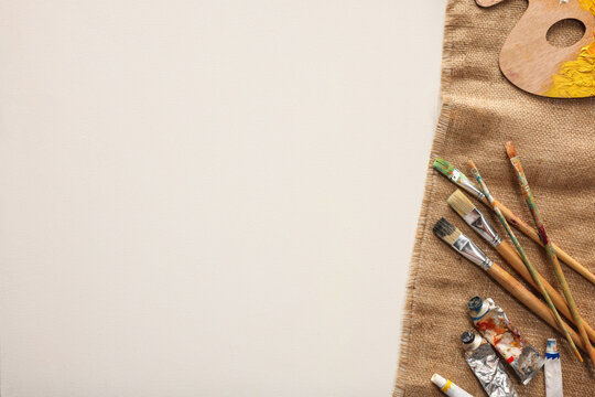 Natural burlap fabric and different painting supplies on white background, top view. Space for text