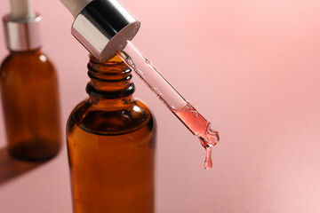 Dripping moisturizing serum from pipette into bottle on pink background, closeup