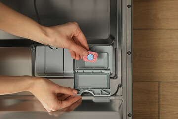 Woman putting detergent tablet into open dishwasher, top view