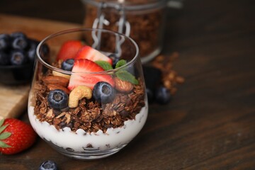 Tasty granola with berries, nuts and yogurt in glass on wooden table, closeup. Space for text
