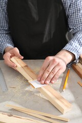 Man polishing wooden plank with sandpaper at grey table, closeup