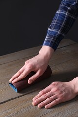 Man polishing wooden table with rolled sheet of sandpaper, closeup