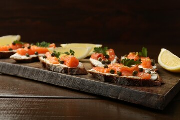 Tasty canapes with salmon, capers, lemon and cream cheese on wooden table, closeup