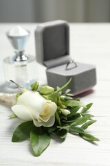 Wedding stuff. Stylish boutonniere, perfume and ring on white wooden table, closeup