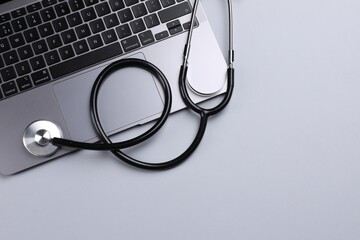 Laptop and stethoscope on light grey background, flat lay. Space for text