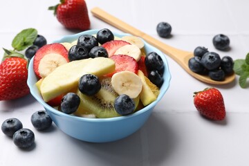 Tasty fruit salad in bowl and ingredients on white tiled table, closeup