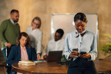 Interracial businesswoman typing messages on phone at meeting at office